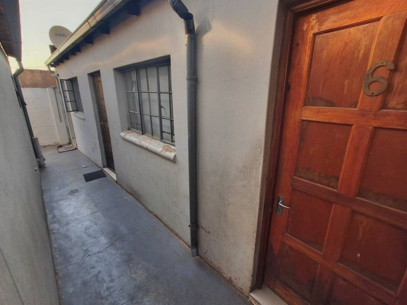 A narrow exterior side passage featuring concrete paving, steel-framed windows, and timber panel doors with visible signs of weathering.