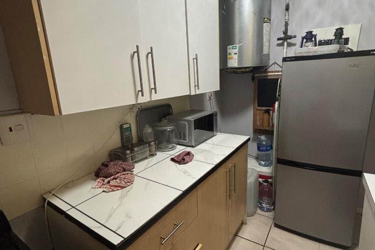 Compact kitchen featuring built-in cabinetry, tiled countertops, and an exposed electric geyser. The space offers functional storage and basic utility fixtures.