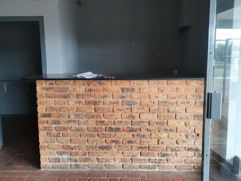 An empty open-plan space featuring a rustic brick breakfast bar and terracotta tile flooring, currently undergoing interior finishing.