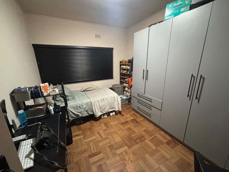 A bedroom featuring classic parquet flooring, a large built-in wardrobe with modern handles, and dark venetian blinds for privacy.