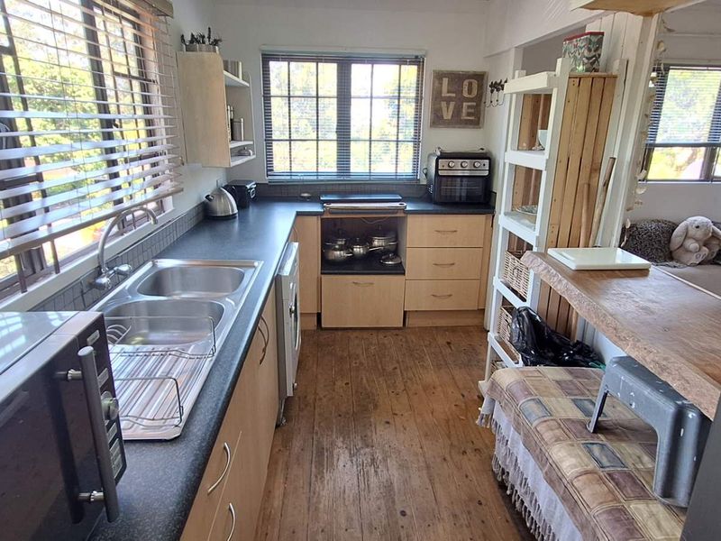 A functional kitchen featuring timber flooring, laminate countertops, and a double bowl stainless steel sink with natural light from multiple windows.