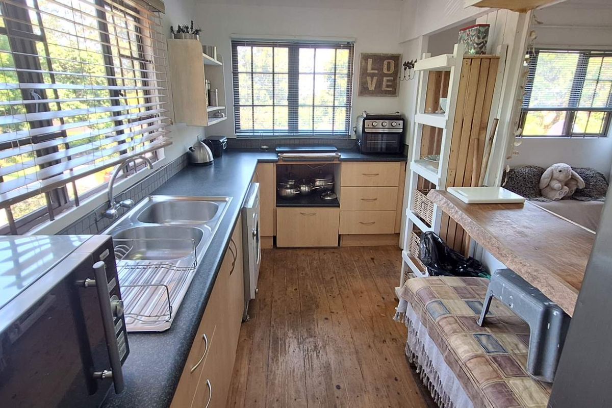 A functional kitchen featuring timber flooring, laminate countertops, and a double bowl stainless steel sink with natural light from multiple windows.
