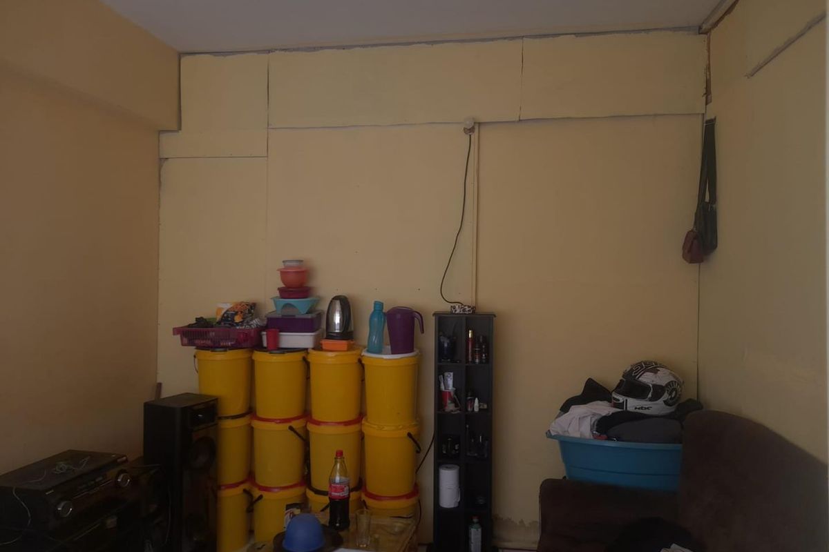 A living area featuring plain yellow walls with visible panel seams and exposed electrical wiring, requiring cosmetic updates and maintenance.