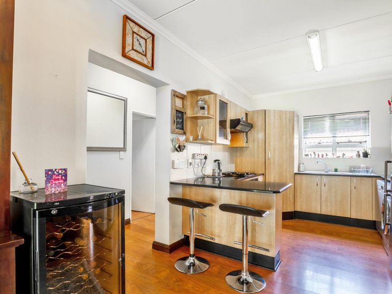 A functional kitchen featuring light wood-finish cabinetry, dark granite countertops, a breakfast bar, and integrated cooking appliances with laminate flooring throughout.