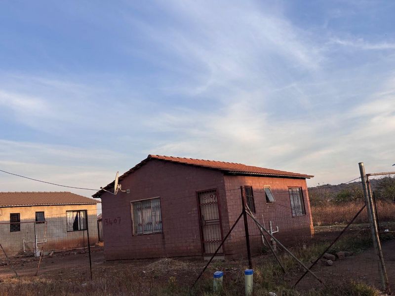 A detached single-story house featuring a tiled roof, security bars on windows, and a gated entrance, situated on an unpaved plot.