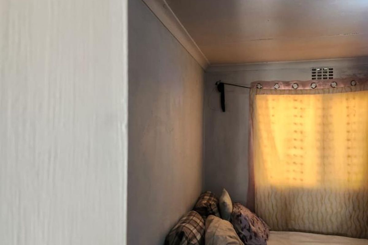 A compact bedroom featuring a window with a curtain rod and simple cornice detailing, requiring cosmetic updates to improve the overall finish.