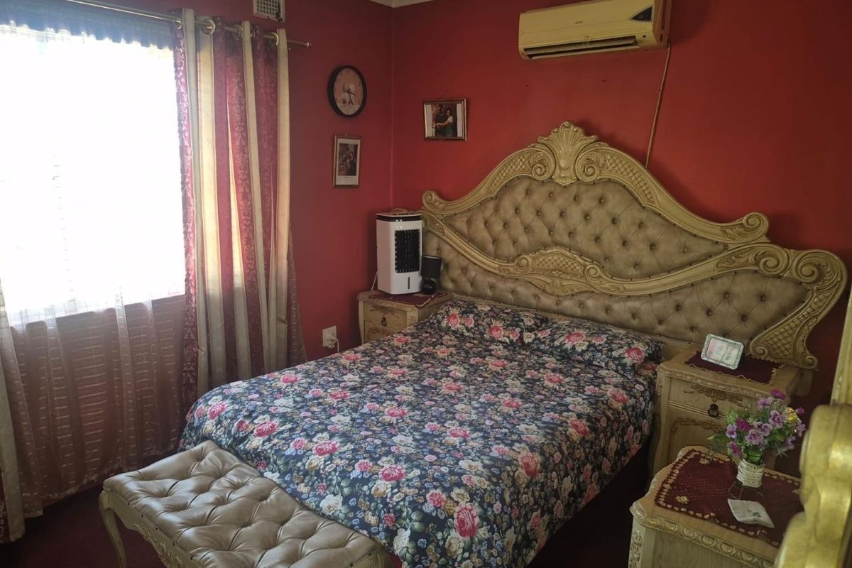 A bedroom featuring a wall-mounted air conditioning unit and a ventilation grille, with red painted walls and a window.