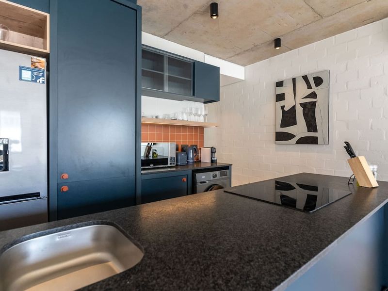 Modern kitchen featuring a central island with stone countertop, induction cooktop, integrated sink, dark cabinetry, and stylish exposed concrete ceiling finishes.
