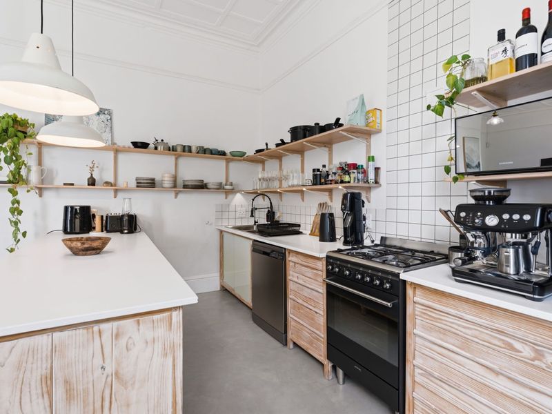 Modern kitchen featuring a central island, gas stove, open shelving, and clean tiled splashbacks, offering a functional and stylish culinary space.