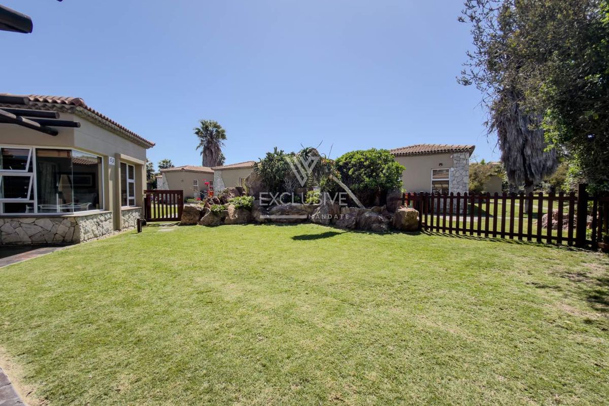 A well-maintained rear garden featuring a manicured lawn, stone landscaping elements, and timber fencing, adjacent to the townhouse structure.