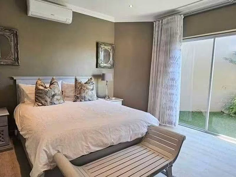 A well-maintained bedroom featuring laminate flooring, recessed lighting, a split-system air conditioner, and large sliding glass doors providing direct access to the garden.