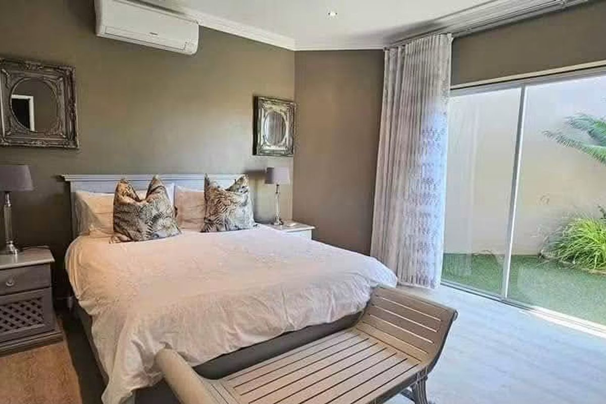 A well-maintained bedroom featuring laminate flooring, recessed lighting, a split-system air conditioner, and large sliding glass doors providing direct access to the garden.