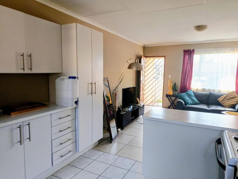 Open-plan living area featuring a functional kitchen with white cabinetry and tiled flooring, leading directly to the main entrance.