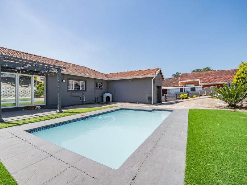 A well-maintained outdoor pool area featuring a swimming pool, a covered pergola patio, and artificial lawn landscaping.