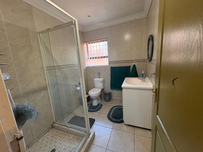 A functional bathroom featuring a glass shower enclosure, vanity basin, toilet, and neutral wall and floor tiling.