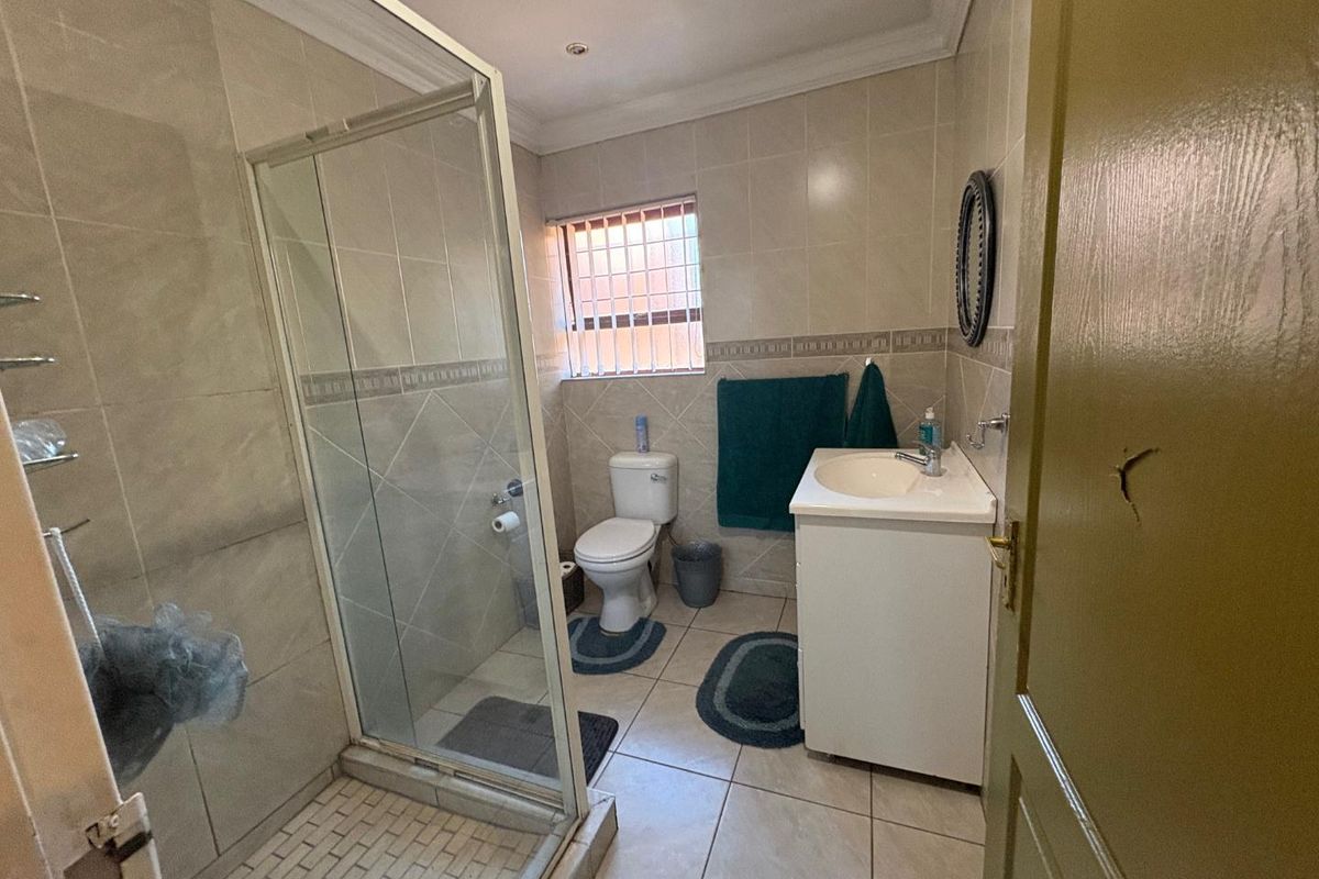 A functional bathroom featuring a glass shower enclosure, vanity basin, toilet, and neutral wall and floor tiling.