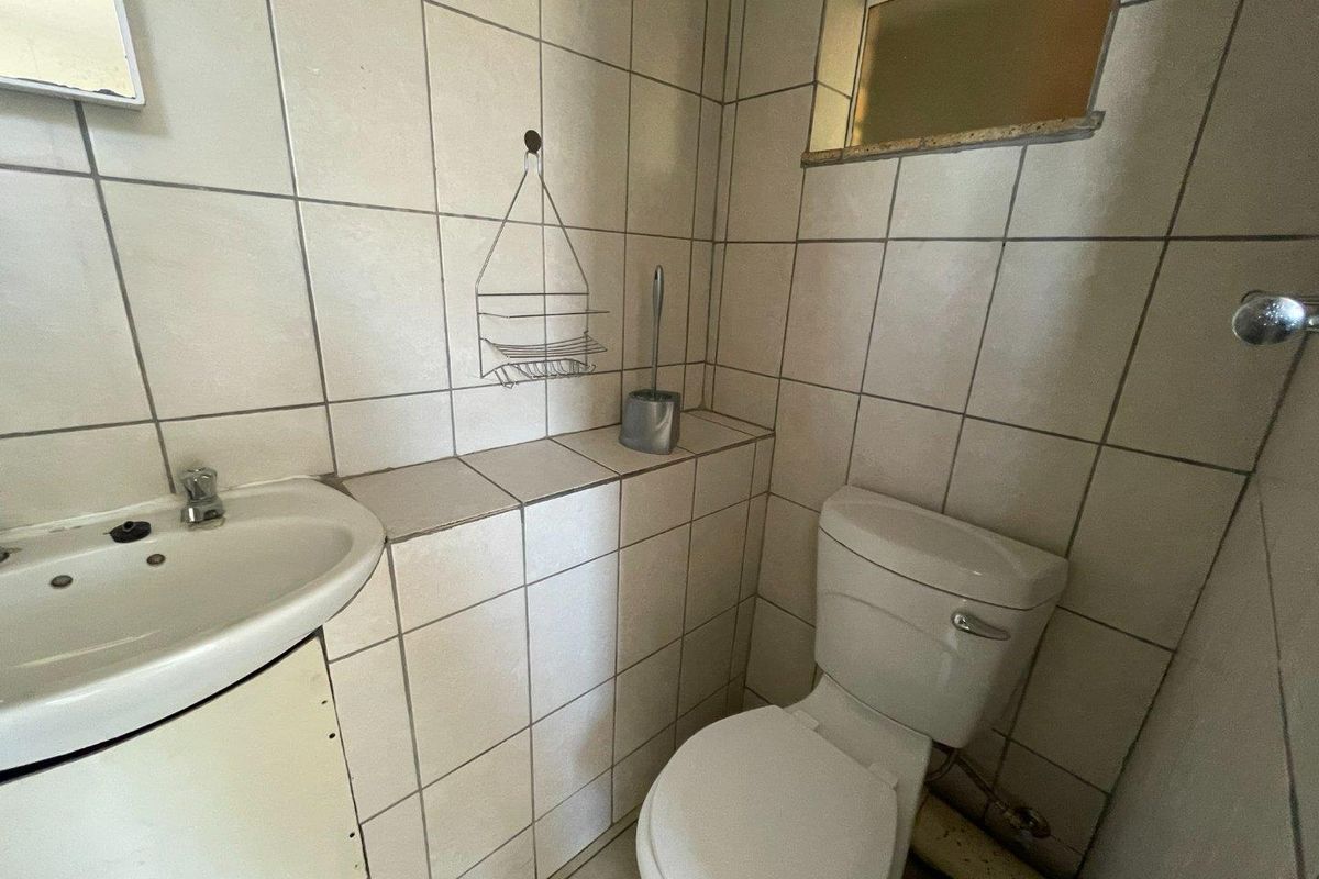 A compact bathroom featuring tiled walls and flooring, a standard toilet, and a wall-mounted vanity basin.