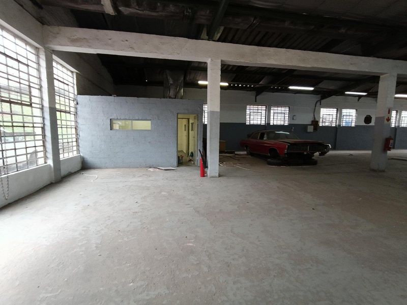 Spacious industrial utility area featuring exposed concrete beams, large steel-framed windows, and a partitioned office enclosure, suitable for workshop or storage use.