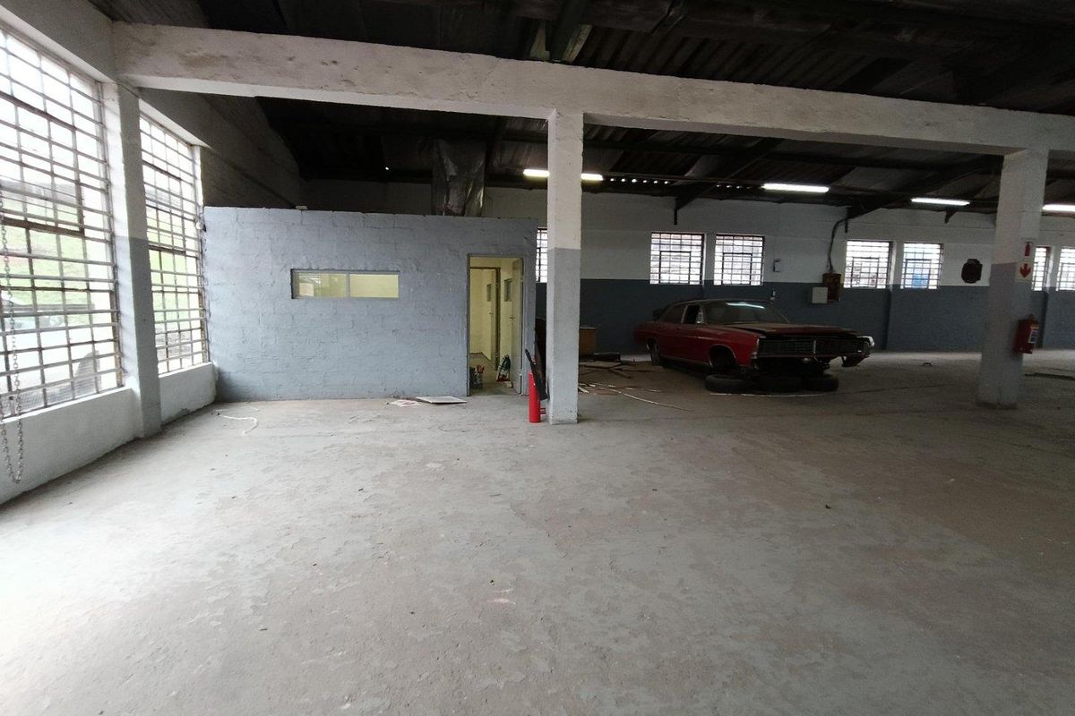 Spacious industrial utility area featuring exposed concrete beams, large steel-framed windows, and a partitioned office enclosure, suitable for workshop or storage use.