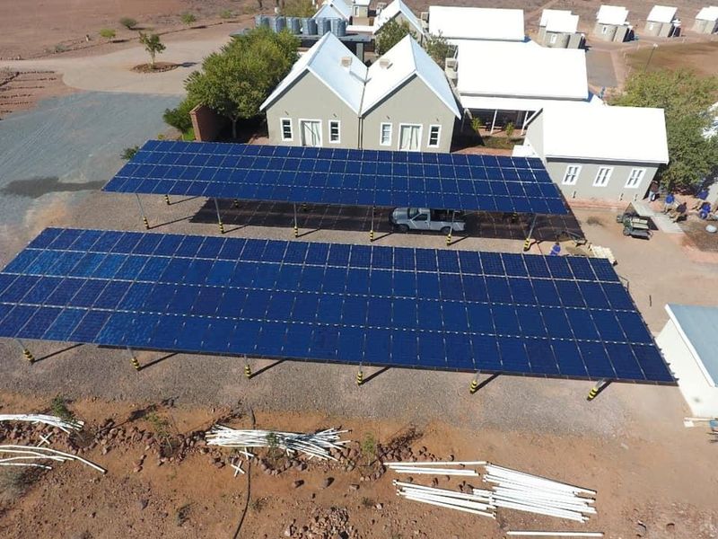 Aerial view of a farm property featuring a large ground-mounted solar panel array providing covered parking for vehicles.