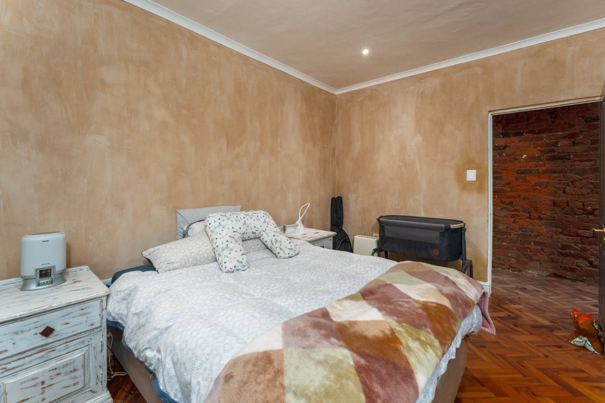 Bedroom featuring parquet flooring, recessed lighting, and a textured wall finish, with an adjacent room showing exposed brickwork.