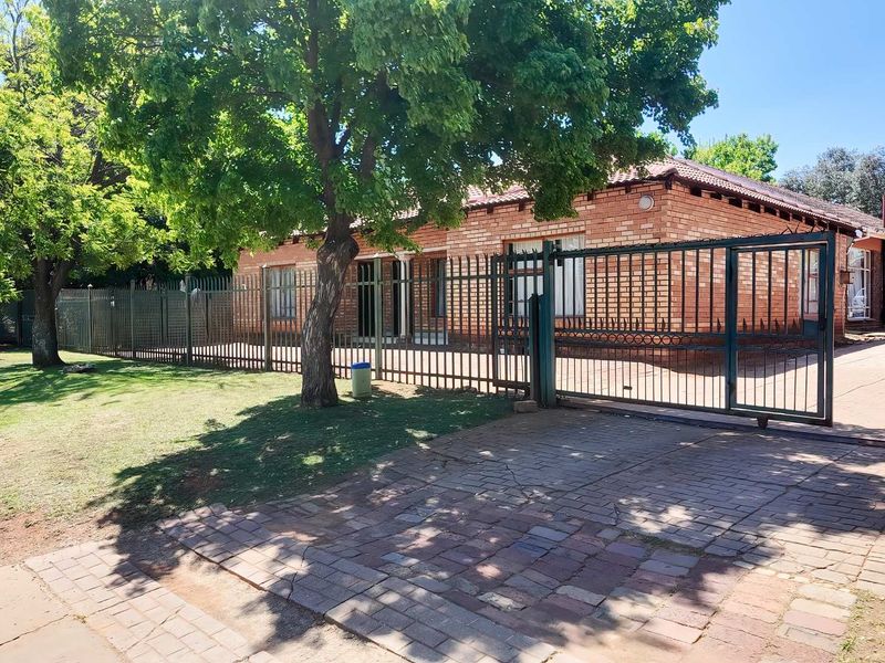 Front view of a face brick house featuring a paved driveway, secure metal gate, and perimeter fencing.