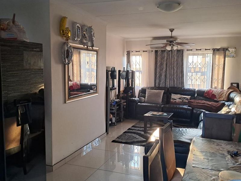 Open-plan living and dining area featuring tiled flooring, a ceiling fan, and natural light through windows fitted with security gates.
