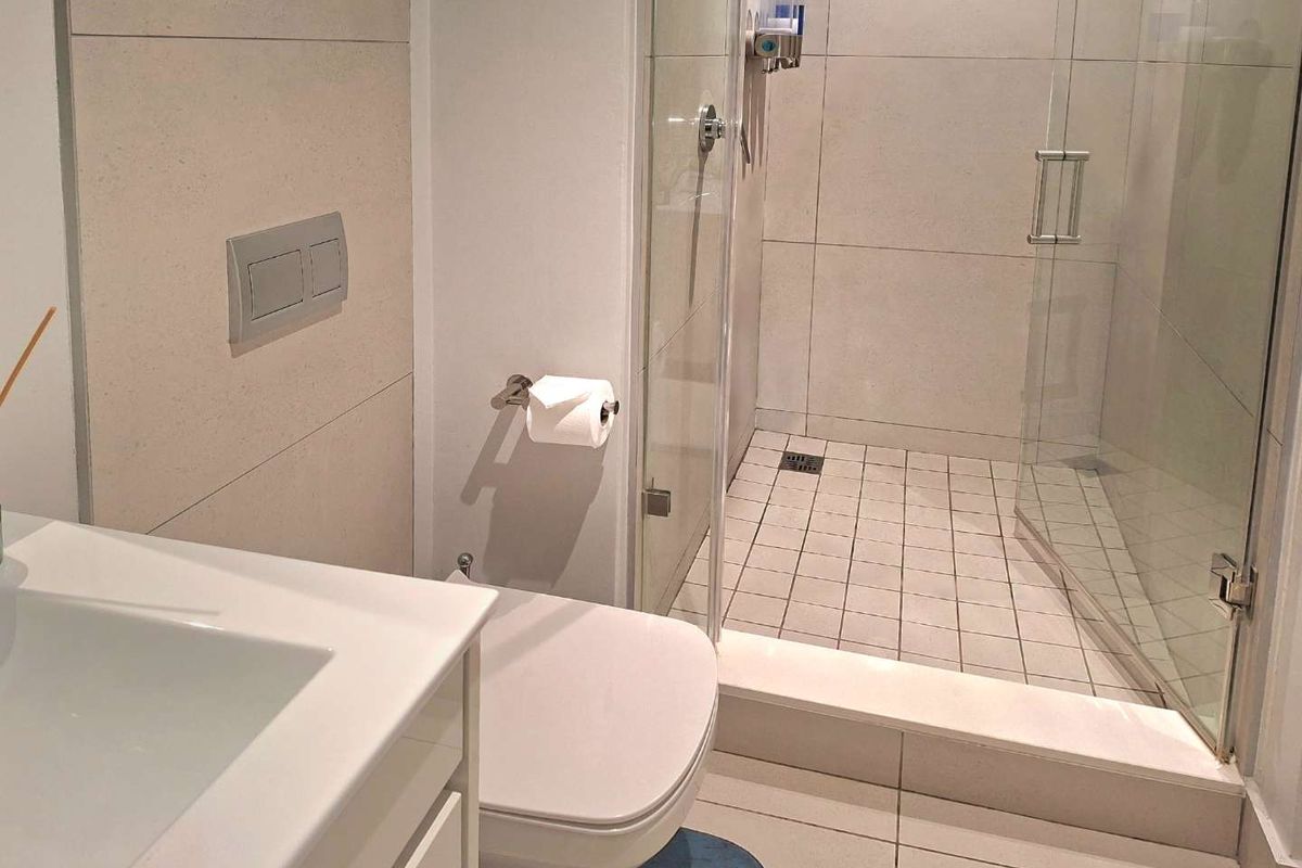Modern bathroom featuring a glass-enclosed shower, wall-mounted toilet with concealed cistern, and a vanity basin with neutral floor and wall tiling.