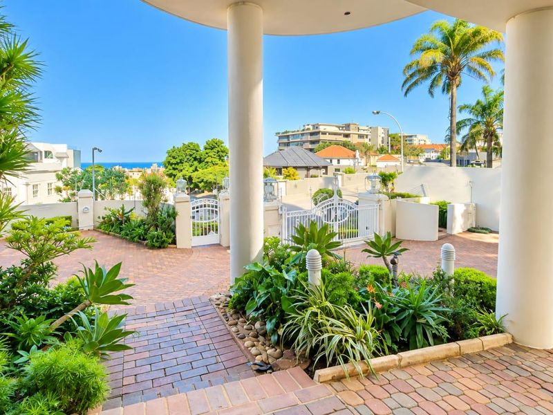 A well-maintained front entrance featuring a brick-paved driveway, secure wrought iron gates, and a covered portico with structural columns.