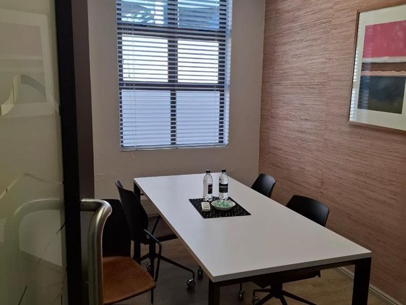 A professional office meeting room featuring wood-look wall paneling, a drop ceiling with recessed lighting, and a glass entrance door.