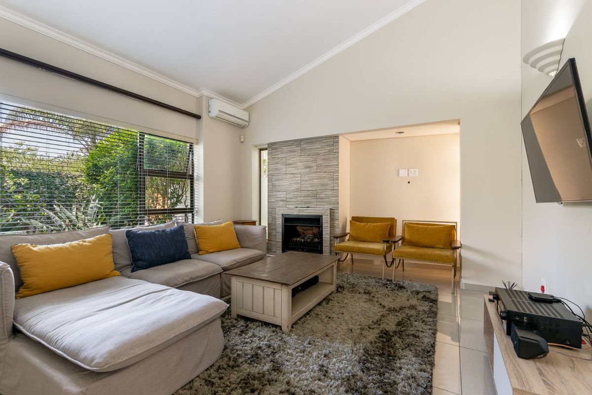 A bright living room featuring a vaulted ceiling, tiled flooring, a modern tiled fireplace, and a wall-mounted air conditioning unit.