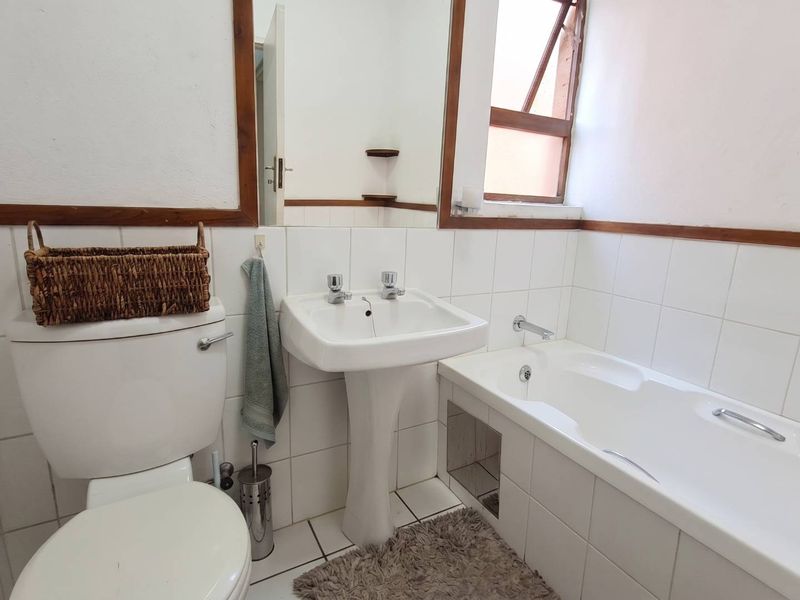 A functional bathroom featuring a white pedestal basin, bathtub, tiled walls, and a wooden-framed mirror, offering a classic layout with natural light.