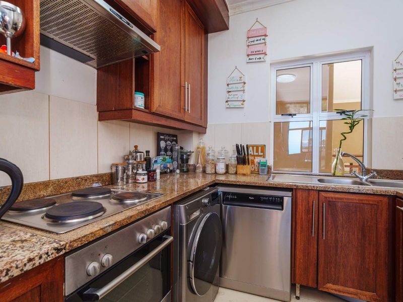 A functional kitchen featuring warm wooden cabinetry, granite countertops, a built-in electric hob, oven, and integrated space for laundry and dishwashing appliances.