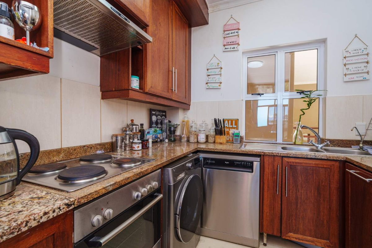A functional kitchen featuring warm wooden cabinetry, granite countertops, a built-in electric hob, oven, and integrated space for laundry and dishwashing appliances.