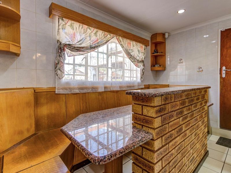 A kitchen breakfast nook featuring a brick-based granite countertop, built-in wooden bench seating, and tiled wall finishes.