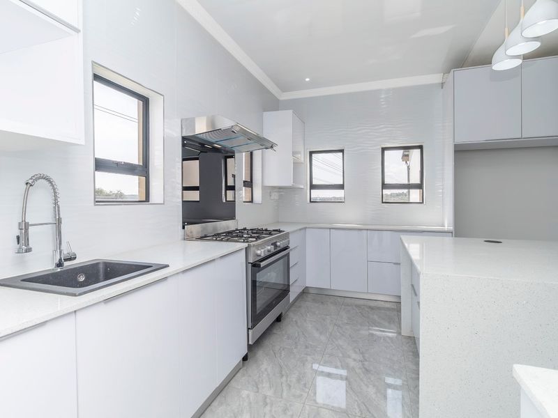 Modern, bright kitchen featuring sleek white cabinetry, quartz countertops, high-end gas stove, and contemporary porcelain floor tiles in a clean, minimalist design.