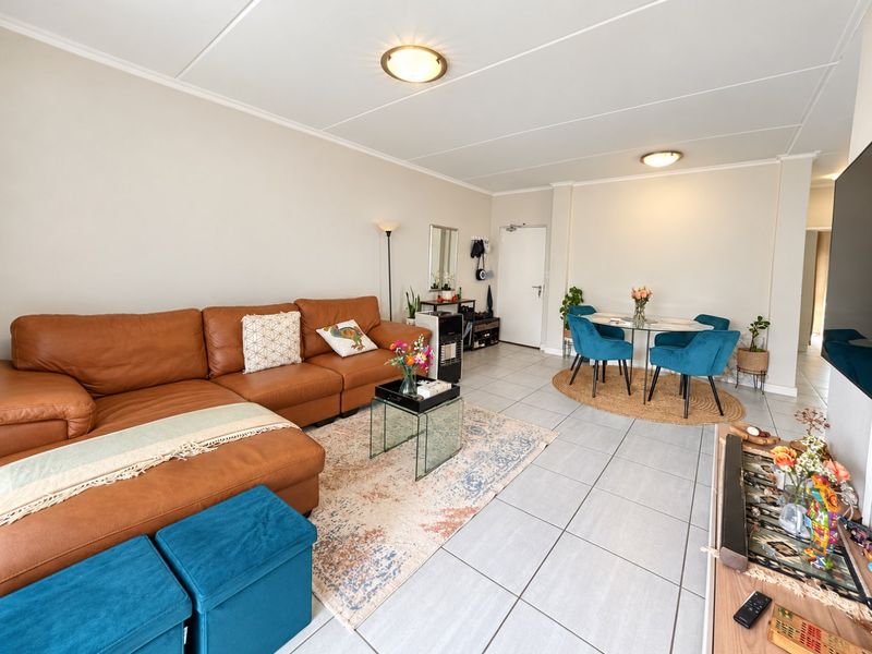 Spacious open-plan living and dining area featuring neutral wall finishes, large format floor tiles, and bright, functional overhead lighting.