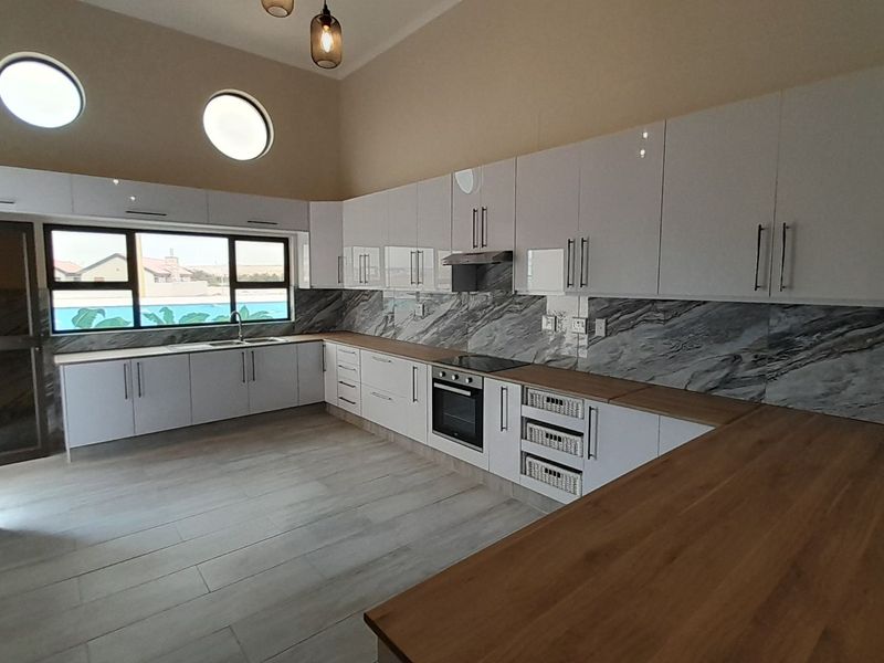 Modern kitchen featuring high-gloss white cabinetry, marble-look splashbacks, wooden countertops, built-in oven, extractor fan, and unique porthole windows.