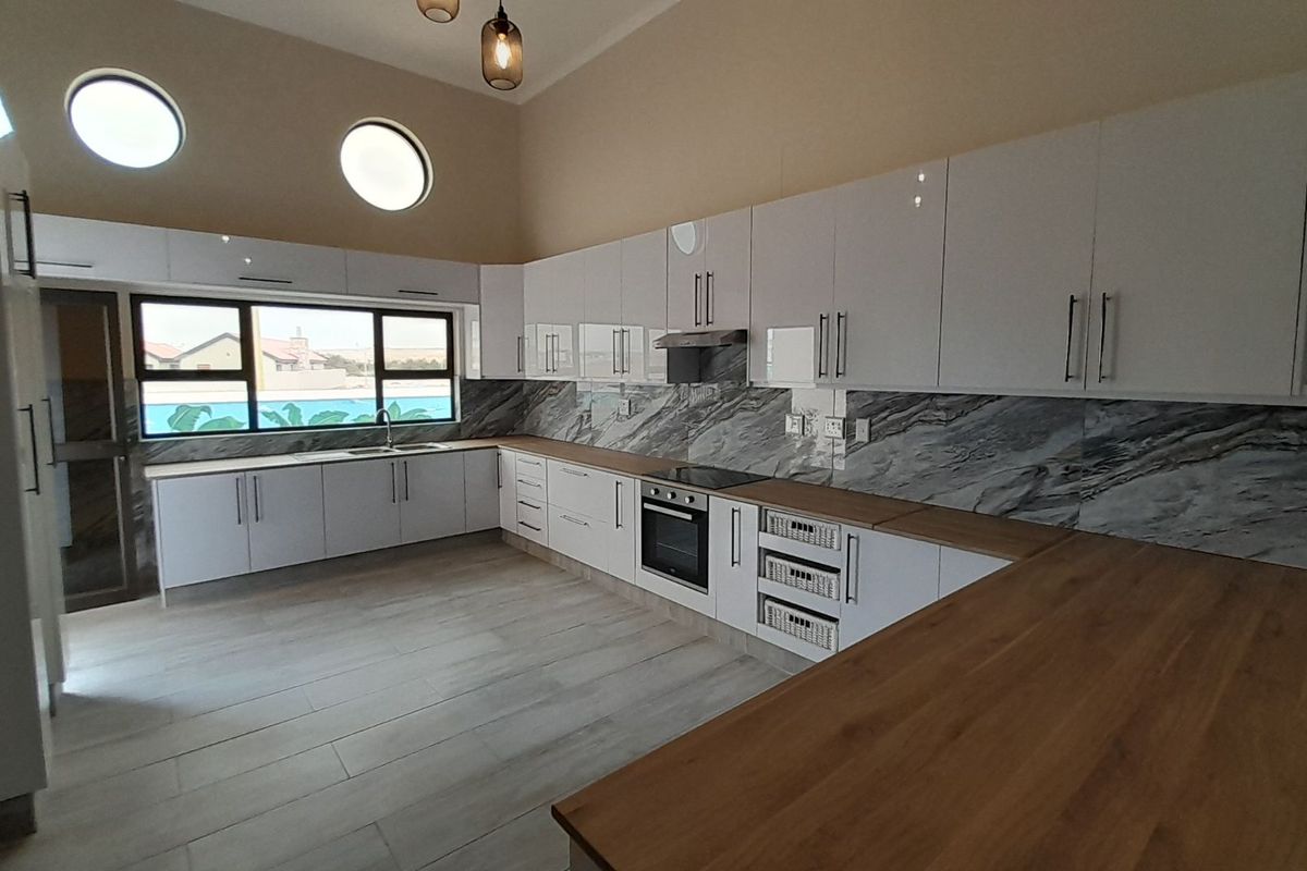 Modern kitchen featuring high-gloss white cabinetry, marble-look splashbacks, wooden countertops, built-in oven, extractor fan, and unique porthole windows.
