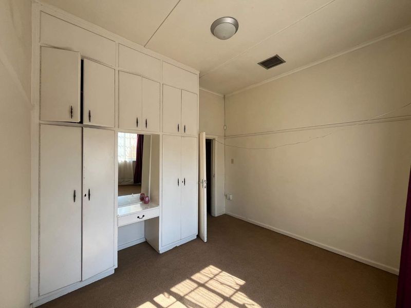 A spacious bedroom featuring extensive built-in cupboards with an integrated vanity mirror, carpeted flooring, and neutral wall finishes.