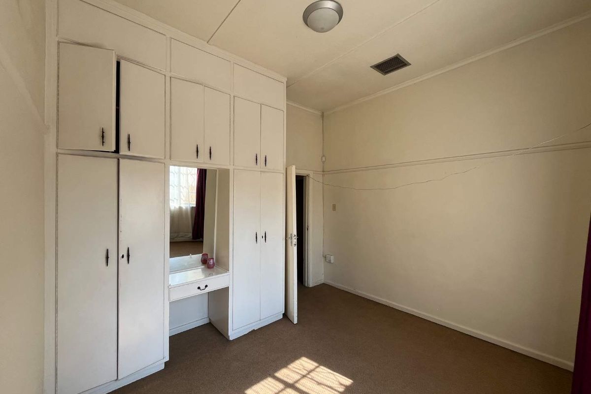 A spacious bedroom featuring extensive built-in cupboards with an integrated vanity mirror, carpeted flooring, and neutral wall finishes.