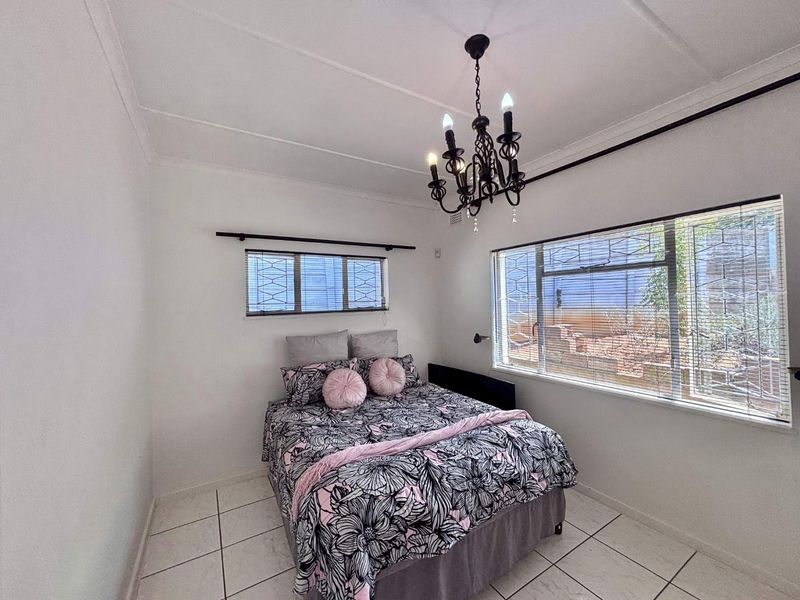 A bedroom featuring tiled flooring, security bars on the windows, and a decorative chandelier.