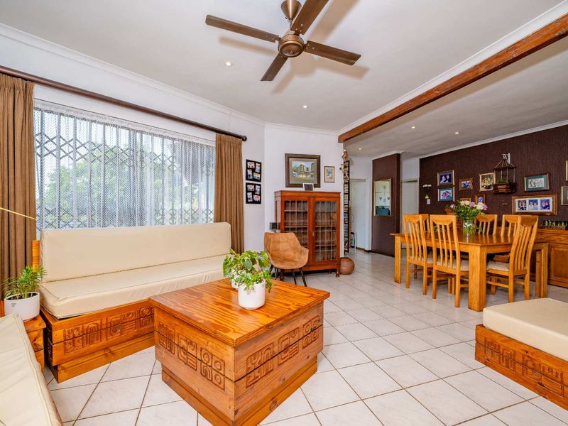 Spacious open-plan living and dining area featuring tiled flooring, a ceiling fan, and large windows with security gates.