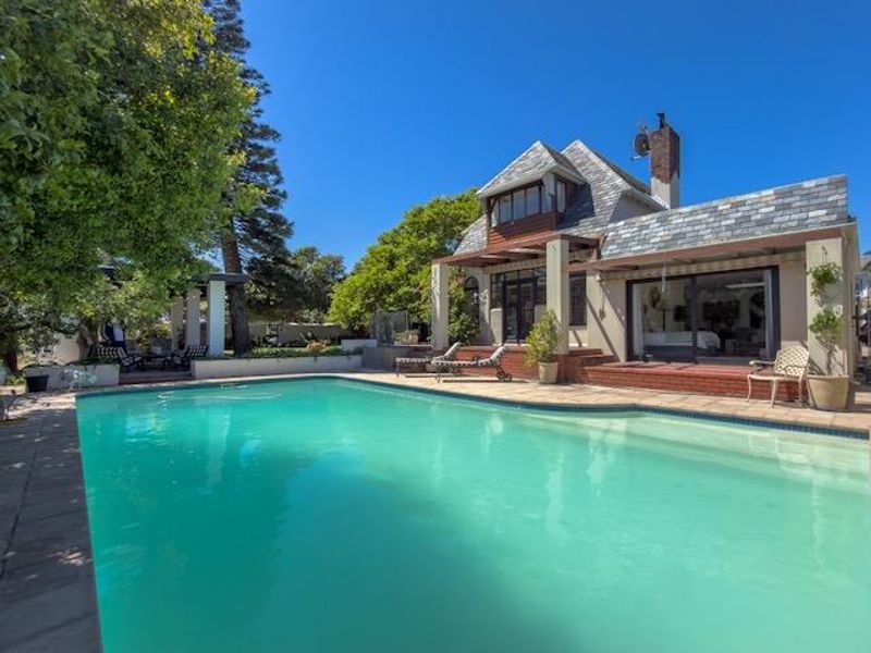 A well-maintained swimming pool area featuring a brick patio, timber pergola, and direct access to the residence through sliding glass doors.