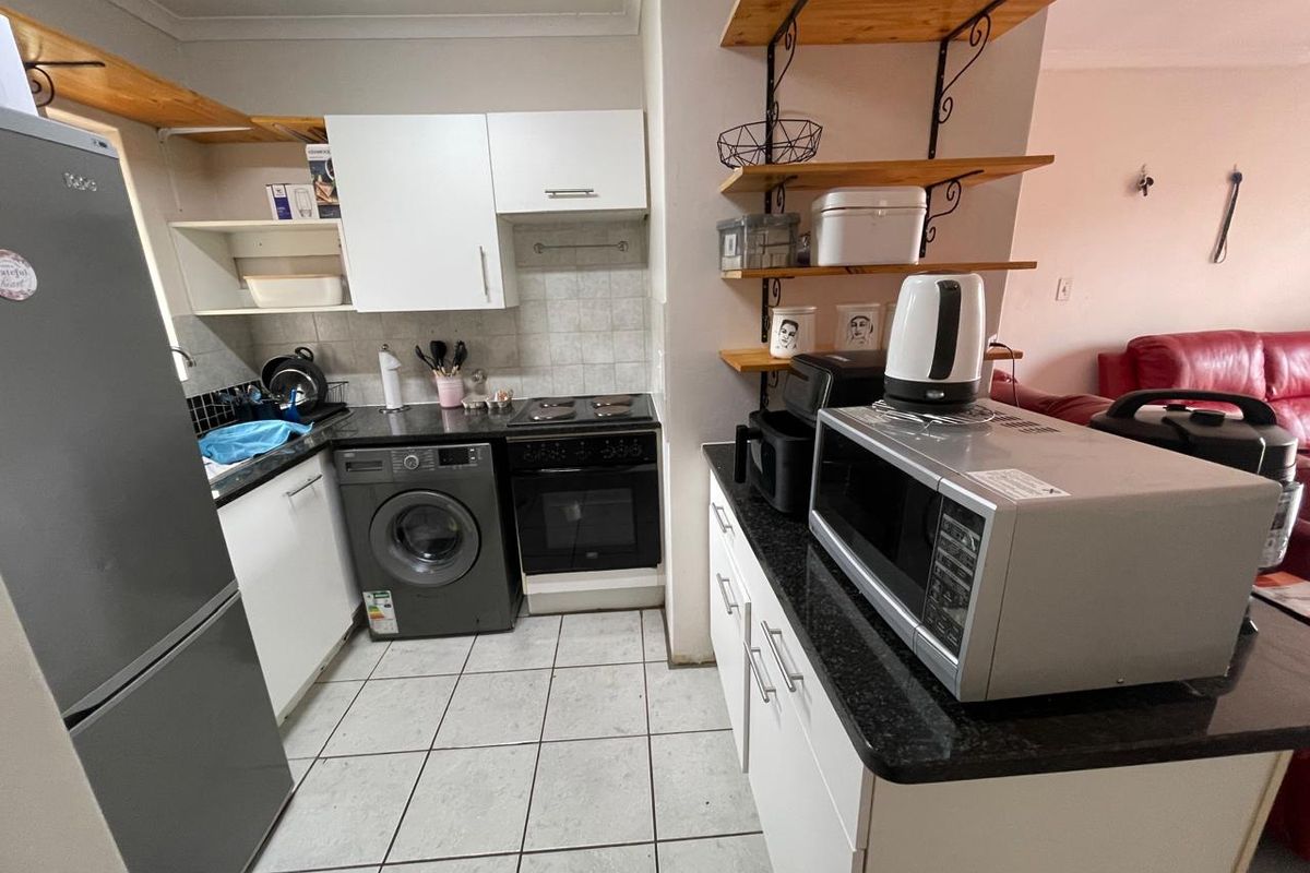 Compact kitchen featuring granite countertops, built-in oven with hob, integrated washing machine space, and open shelving, seamlessly connecting to the living area.