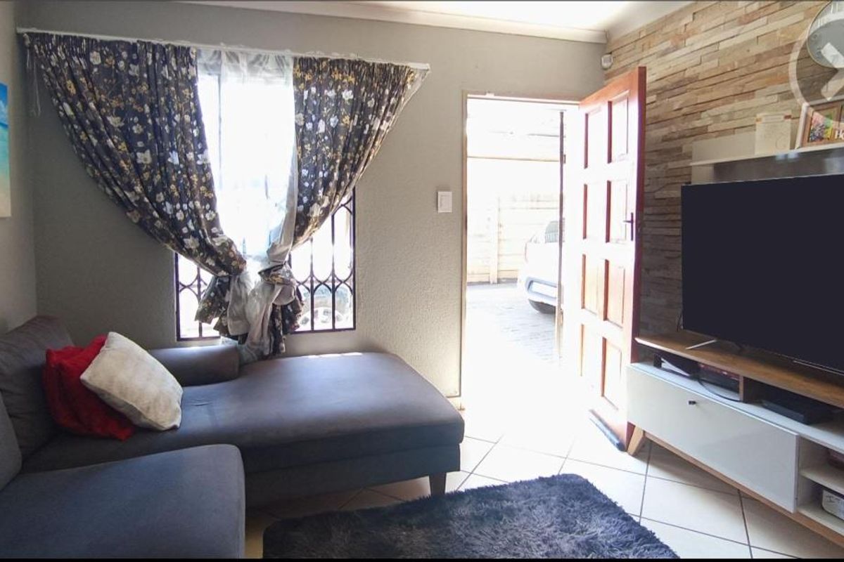 A living room featuring tiled flooring, a stone-cladding feature wall, and direct access to the exterior driveway.