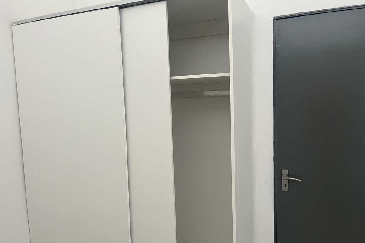 A bedroom featuring a white built-in sliding door wardrobe with internal shelving and hanging space, alongside a dark grey internal door.