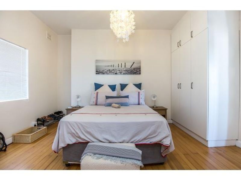 A well-maintained bedroom featuring polished hardwood flooring, ample built-in cupboard storage, and natural light through venetian blinds.
