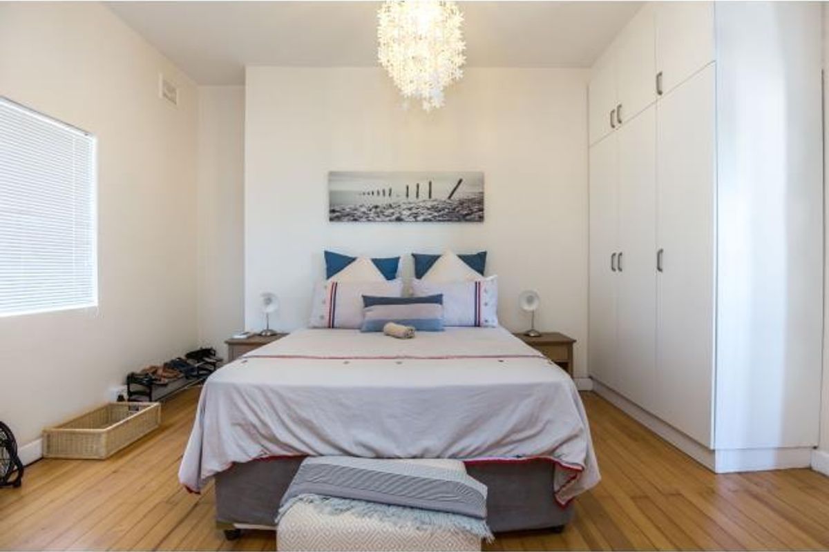 A well-maintained bedroom featuring polished hardwood flooring, ample built-in cupboard storage, and natural light through venetian blinds.