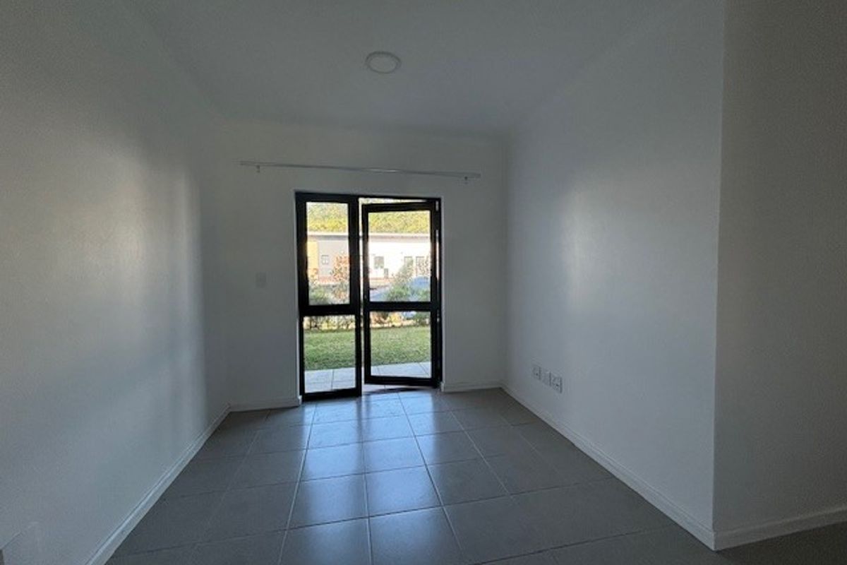 A bright, empty living area featuring neutral tiled flooring and a glass door providing direct access to the outdoor space.